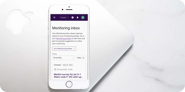 A Mercell monitoring inbox displayed on a white iPhone beside a laptop